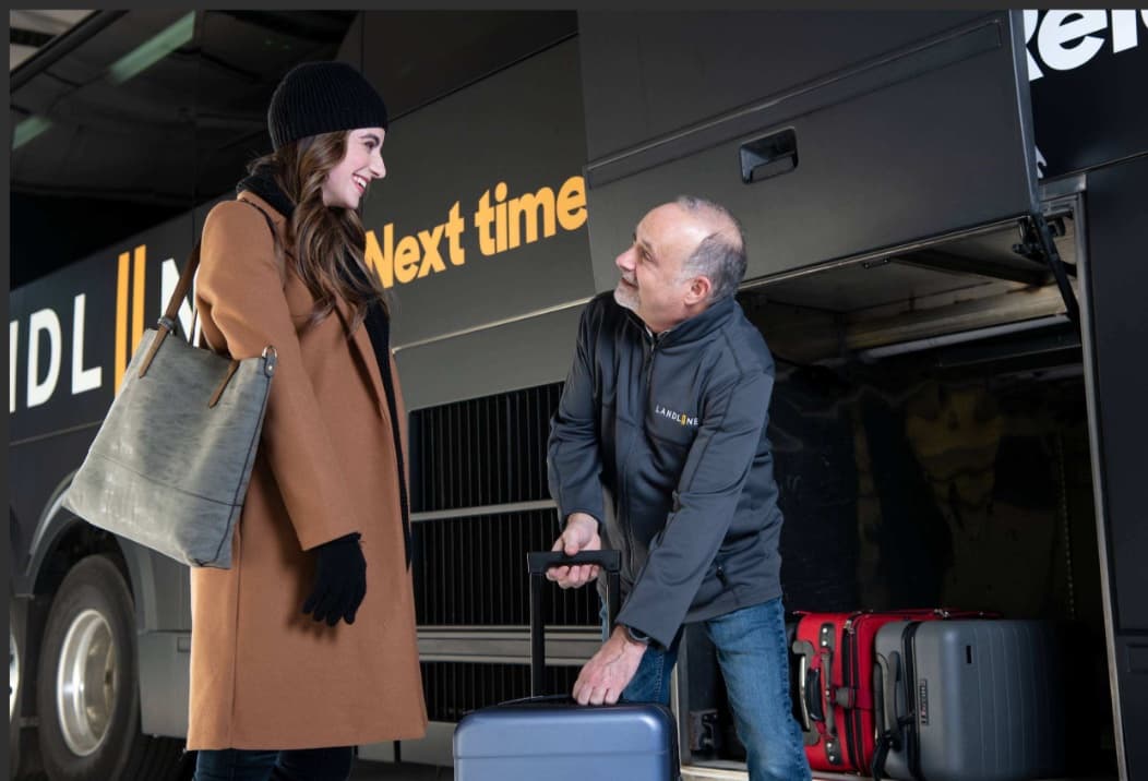 A Landline driver loading a traveler's suitcase into the coach's luggage bay.